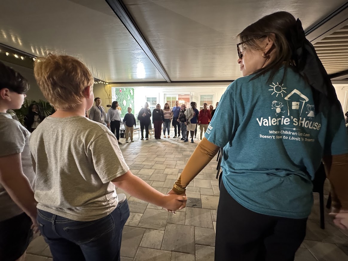 Volunteer and child hold hands in a circle during a Valerie’s House group night activity.