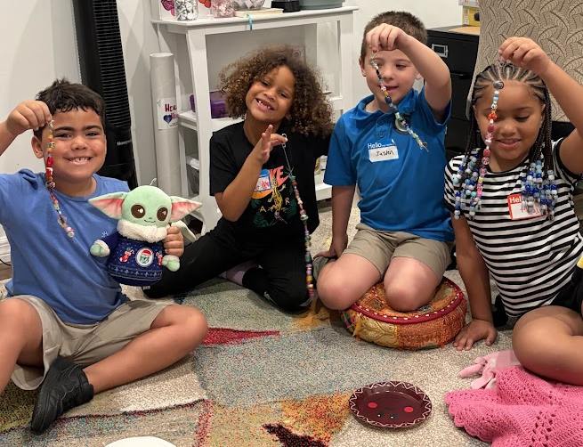 Kids holding beaded crafts during a group night at Valerie’s House