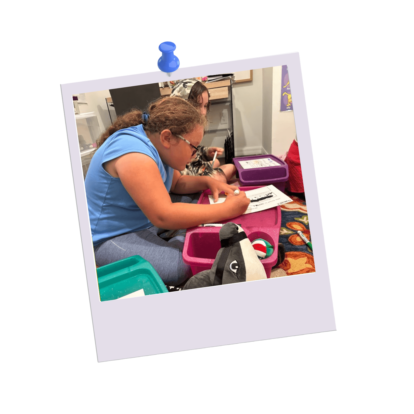 Child at Valerie’s House writing during a group night activity using a lap desk and markers